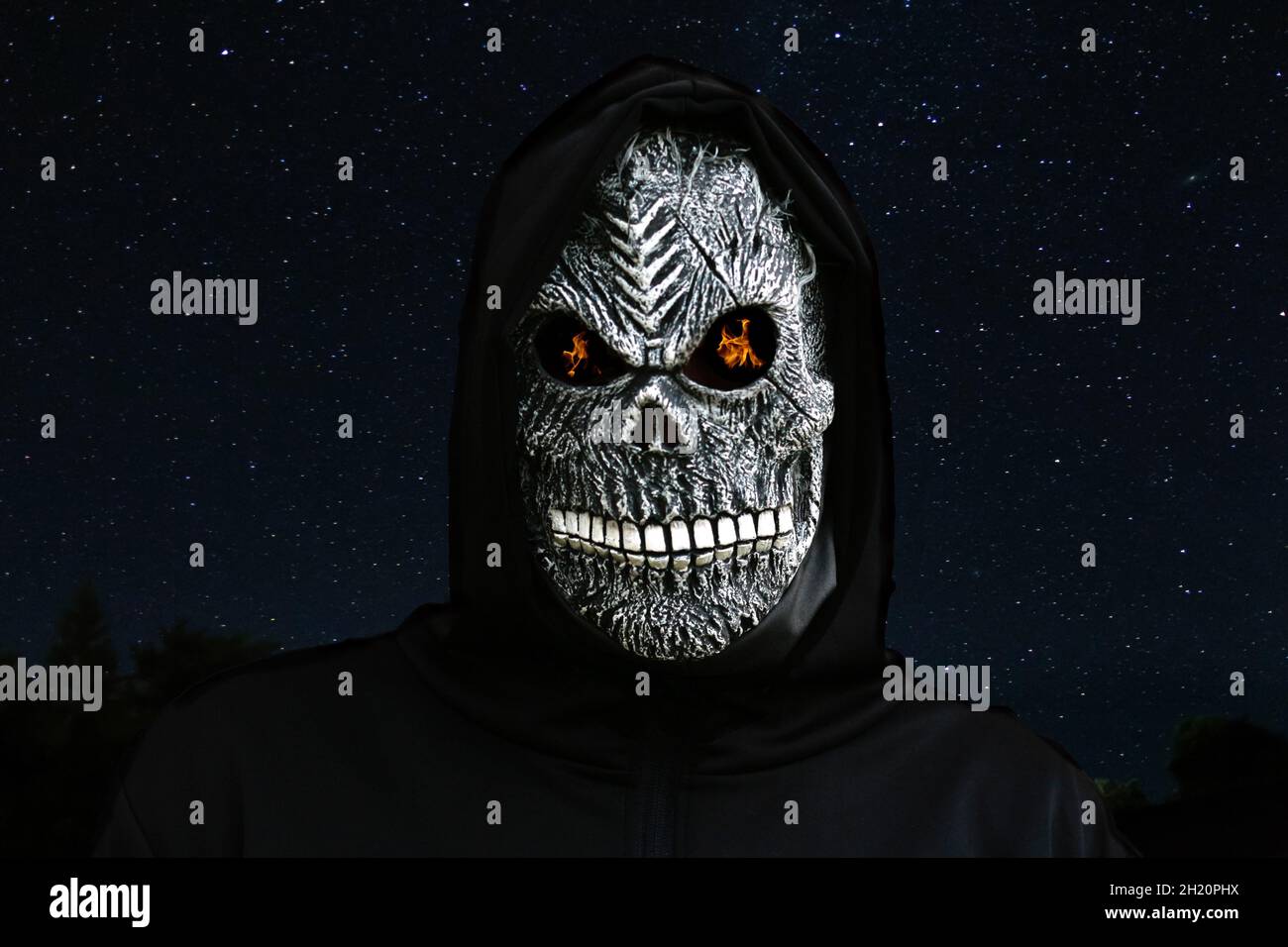 Nahaufnahme des grimmigen Reaper. Mann in Todesmaske mit Feuerflamme in den Augen auf Nachthimmel starren. Faschingskostüm, gruselige Zähne. Halloween-Urlaub Stockfoto