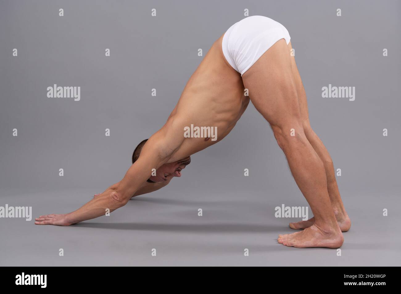 Yogi Mann tun nach unten Hund Adho Mukha Svanasana Yoga stehend stellen grauen Hintergrund, Asana Stockfoto