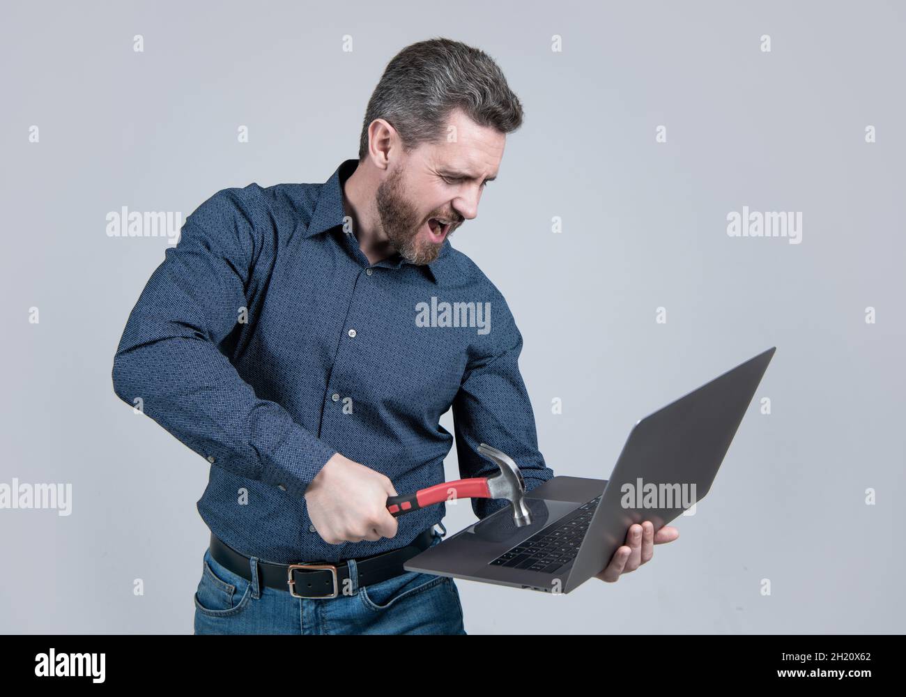 Unkontrollierter Zorn. Verrückter Mann schlug mit Hammer auf den Laptop. Frustriert und verrückt Stockfoto