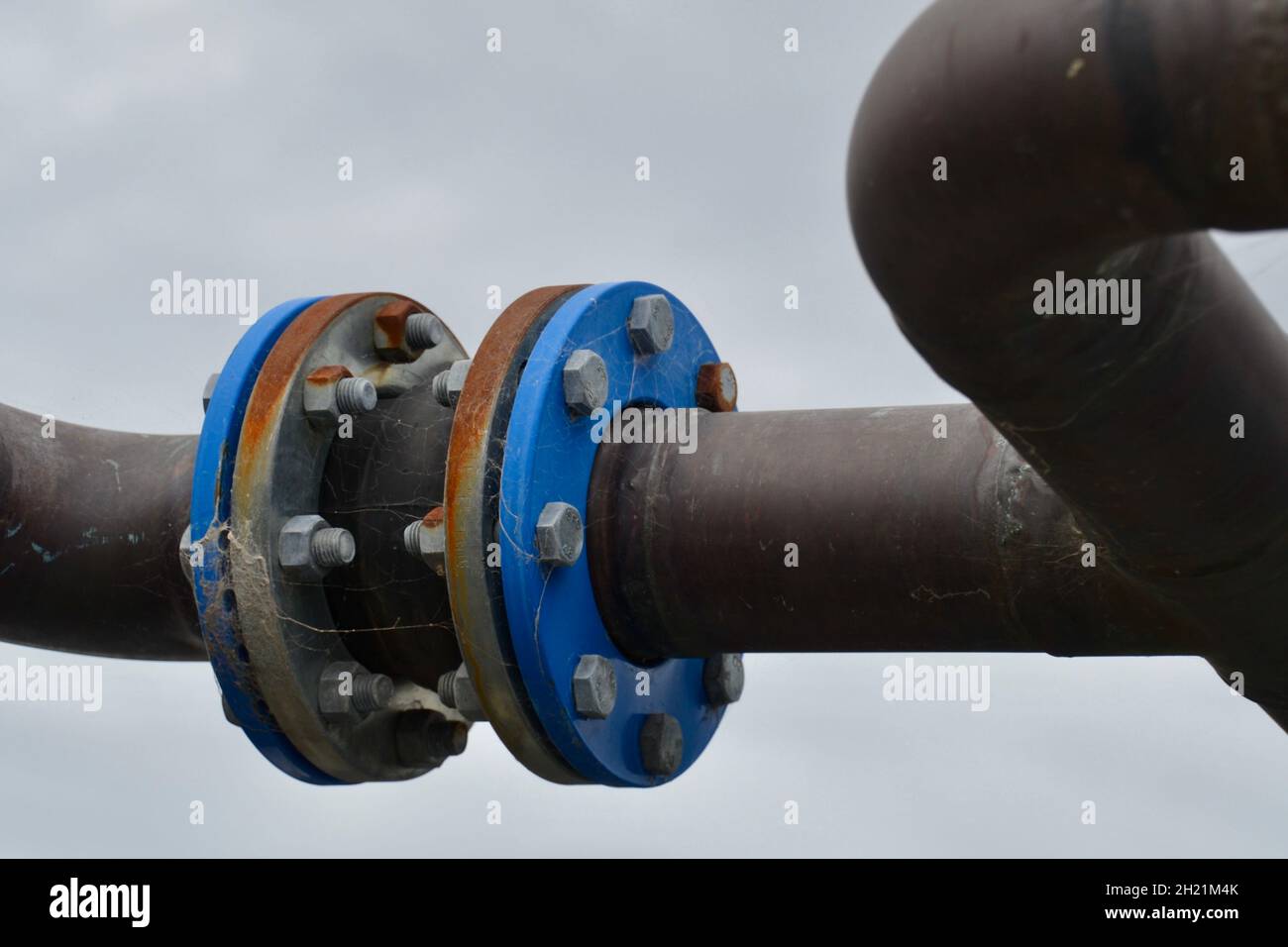 Stahl- oder Kupferrohrsystem für kaltes Kühlwassersystem für Klimaanlagen mit Flanschen im Freien, die Rost und Spinnweben zeigen Stockfoto