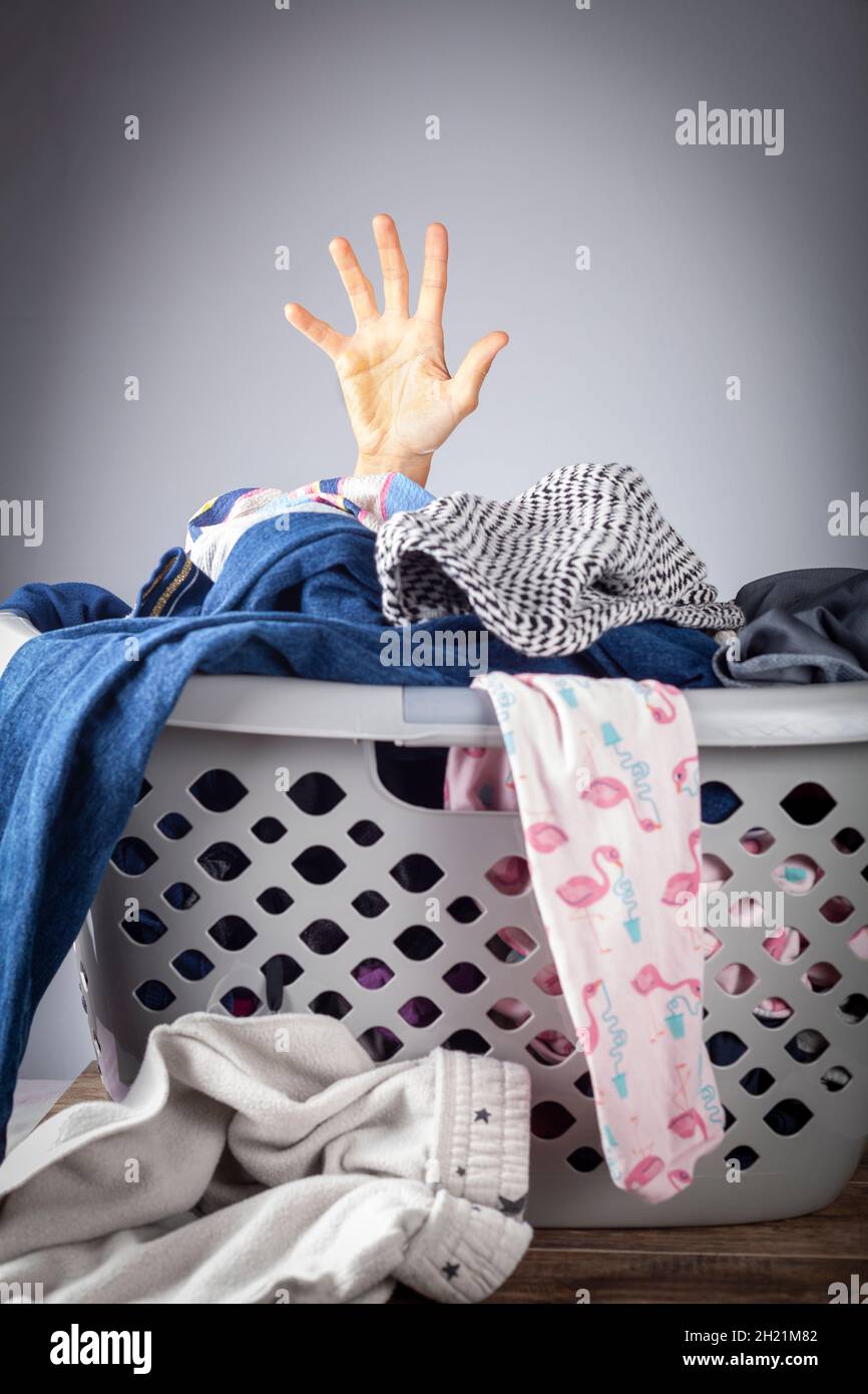 Abstraktes Konzeptbild mit der Hand einer Frau, die aus einem Korb voller Kleidung für die Wäsche kommt. Sie ist überwältigt und gelangweilt von der Hausarbeit und braucht h Stockfoto