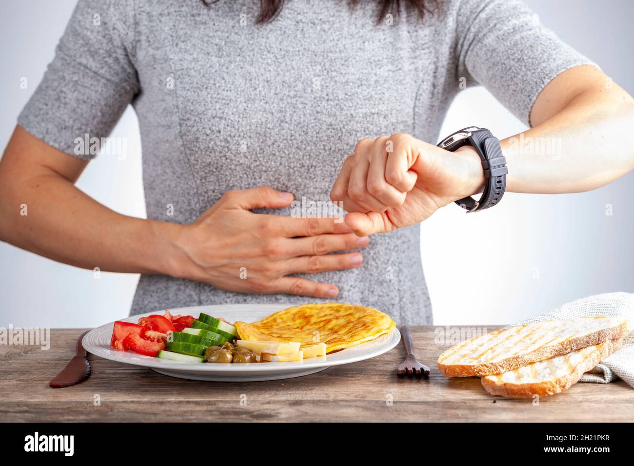 Intermittierendes Fasten-Konzept mit einer Frau, die hungrig vor dem Essen sitzt und ihre Uhr anschaut, um sicherzustellen, dass sie zur richtigen Zeit schnell bricht. A Stockfoto