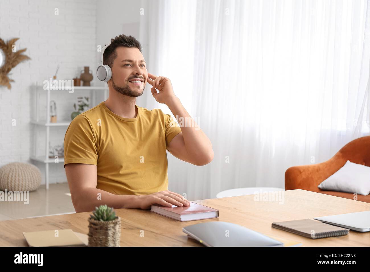 Mann mit Kopfhörern hört Hörbuch am Tisch Stockfoto