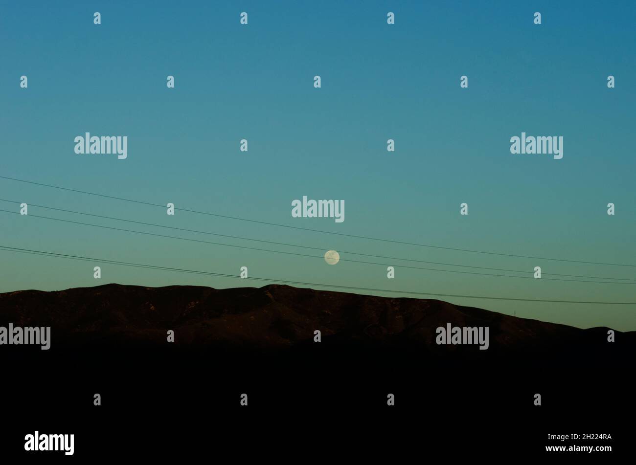Der Mond steigt über den Bergen in Südkalifornien, wobei die Stromleitungen im Vordergrund verlaufen. Stockfoto