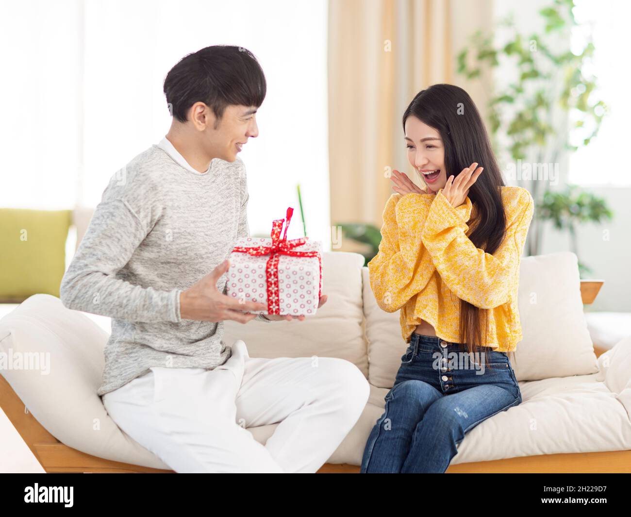 Junger Mann, der der Frau im Wohnzimmer ein Überraschungsgeschenk gibt. Stockfoto