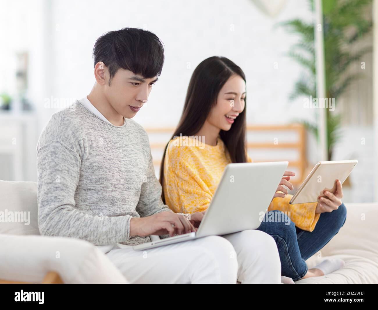 Junges Paar, das im Büro einen Laptop benutzt und sich zu Hause Filme auf dem Sofa ansieht Stockfoto