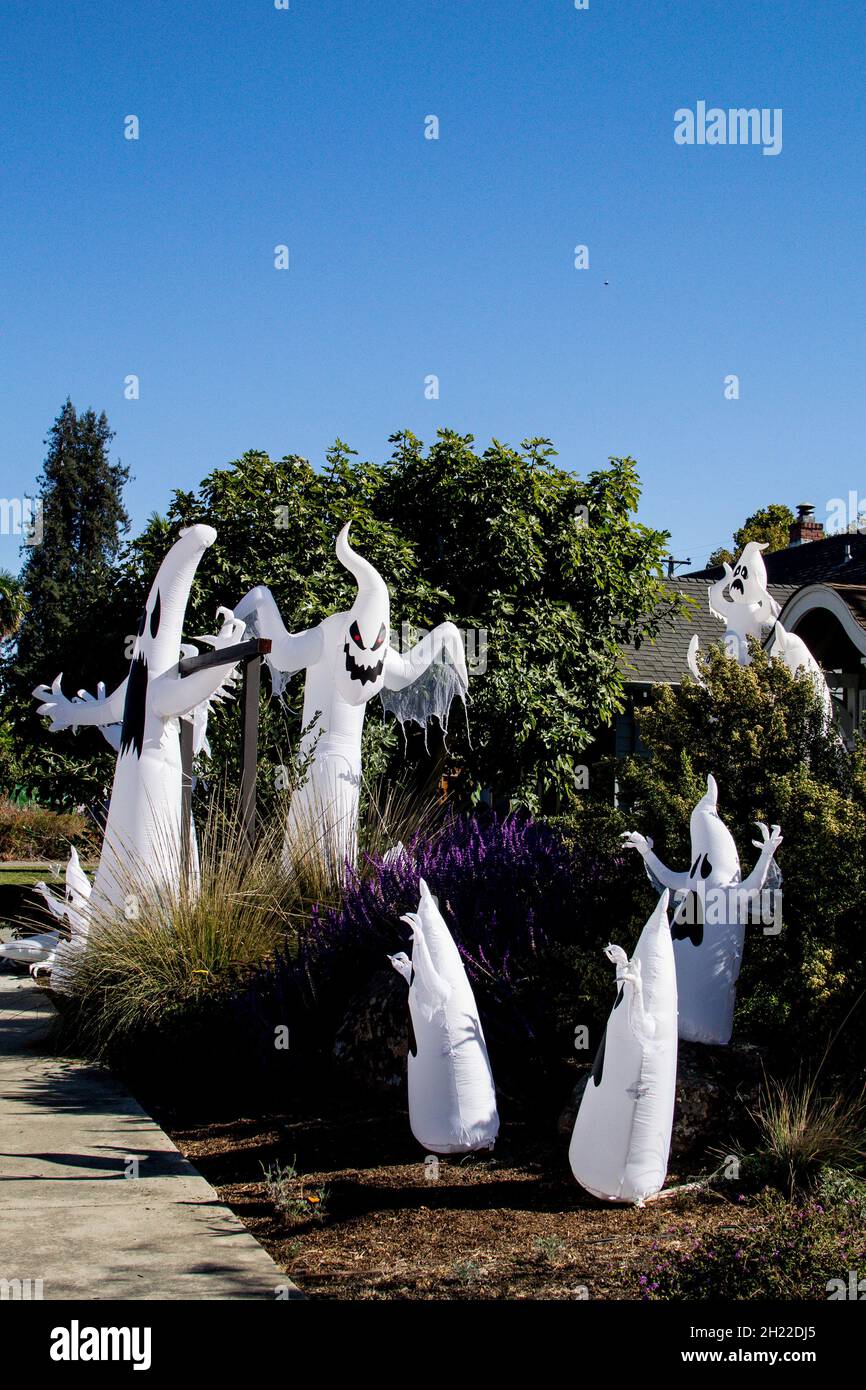 Große Versammlung von mindestens acht luftdurchgeblasenen aufblasbaren Geistern, die auf dem Bürgersteig in einer Wohnstraße im sonnigen Kalifornien zu Halloween-Feiern gegenüberstehen Stockfoto