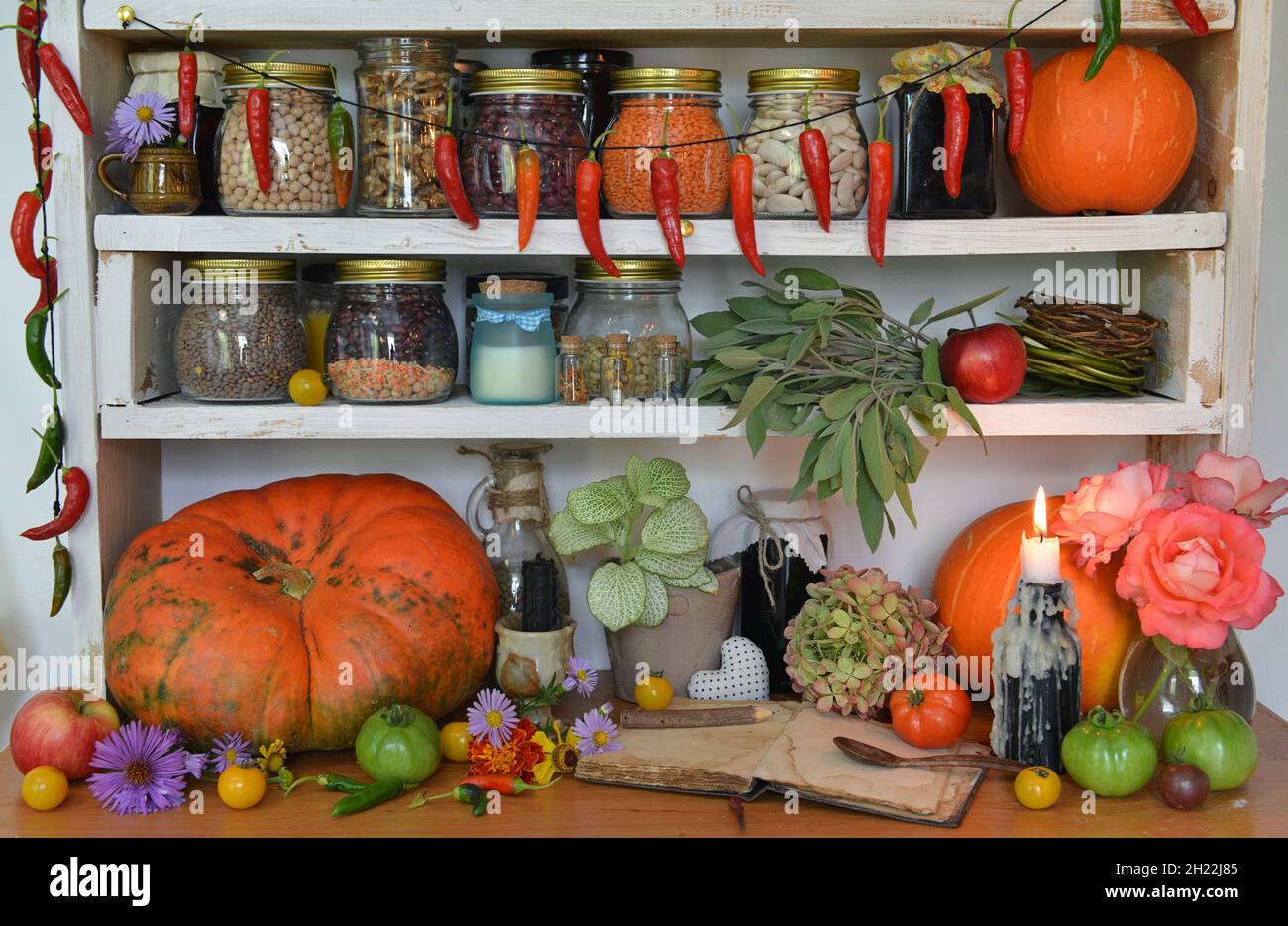 Vintage Küche Stillleben mit brennender Kerze, Bohne in alten Flaschen und Gläser, Kürbis, hängenden Paprika, grüne Tomaten. Provenzalische, ländliche Atmosphäre Stockfoto