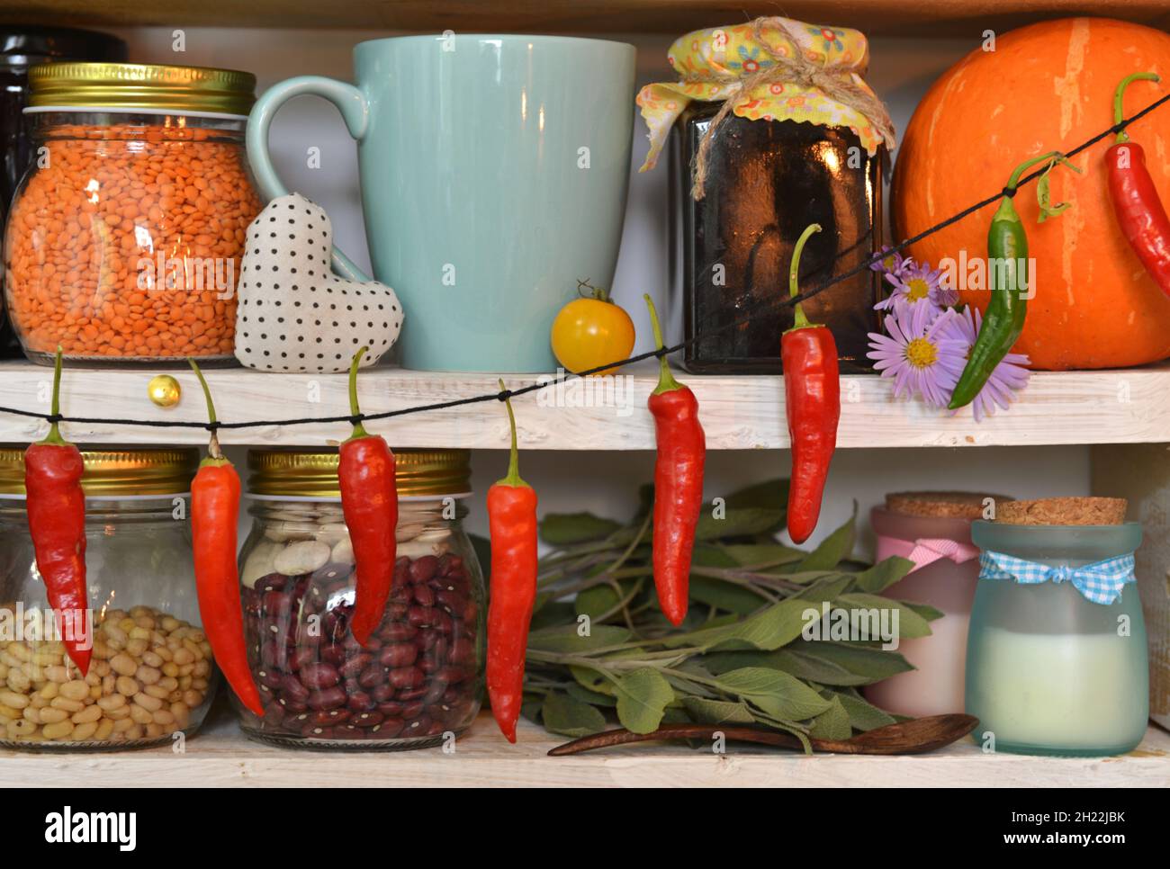 Alte Tasse, Gläser und Flaschen mit Marmelade, Gewürzen und Bohnen, Kürbis und Kräutern auf Holztheke in der Vintage-Küche. Provenzalische, ländliche Atmosphäre Stockfoto