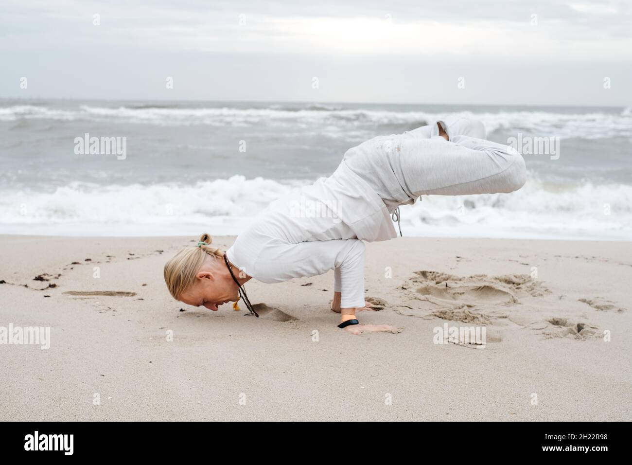 Mann macht Yoga am Strand im Herbst über Wellen im Meer. Cremig, leichter Sand und Himmel, Asanas und Meditation, Gleichgewicht im Leben, Selbstbewusstsein und Stockfoto