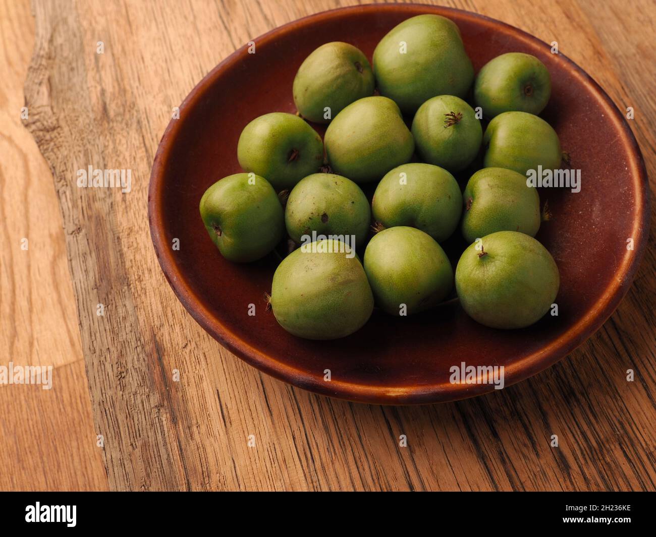 Mini Kiwis (Actinidia arguta) auf einem Steinzeugteller auf einem rustikalen Küchentisch. Gesundes Essen oder Home-Gardening-Konzept Stockfoto
