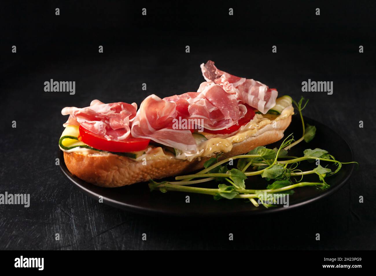 Frisches hausgemachtes Sandwich mit Speck, Gurken und Tomaten auf schwarzem Hintergrund Stockfoto