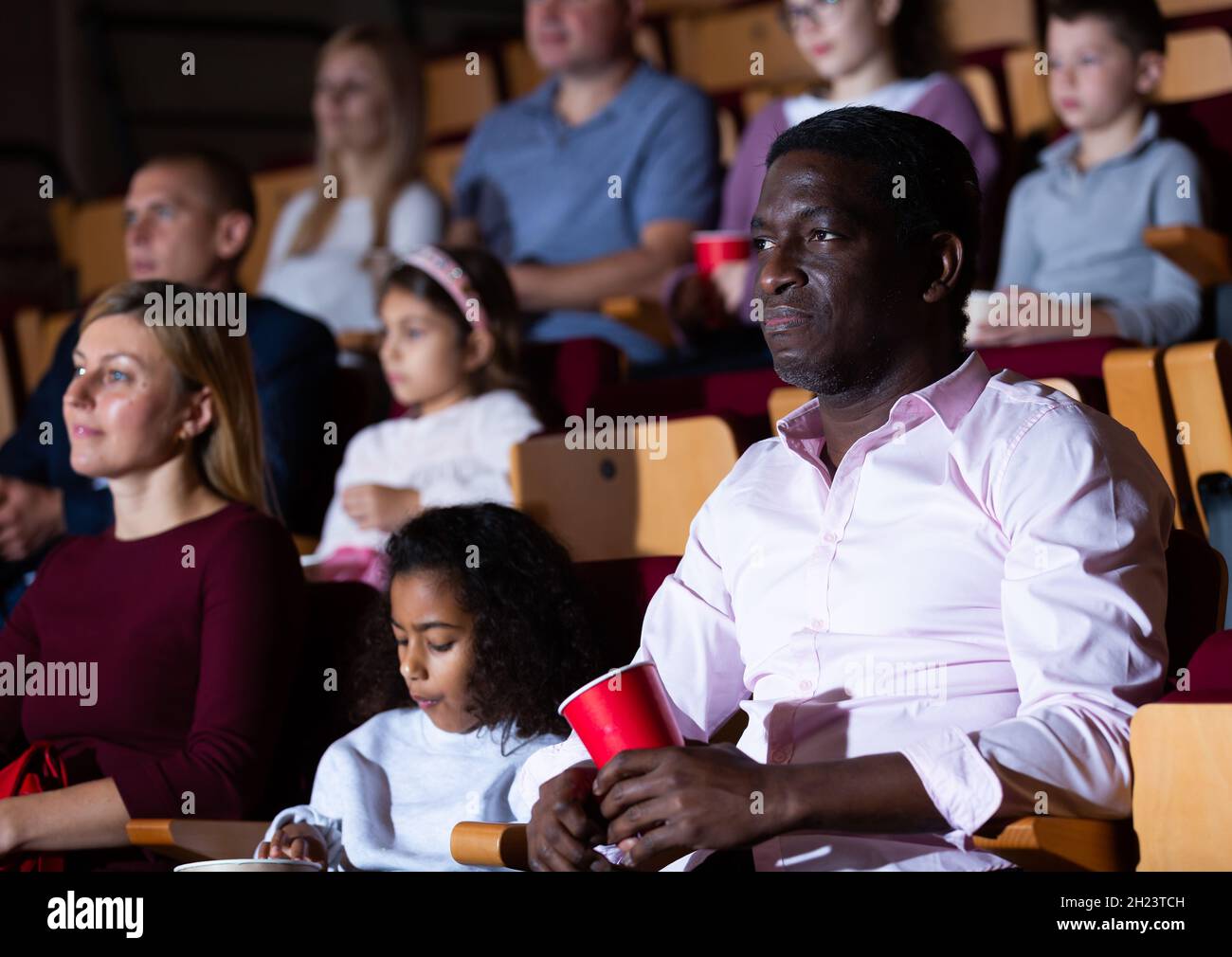 Internationale Familien essen Popcorn und sehen sich Comedy im Kinosaal an Stockfoto
