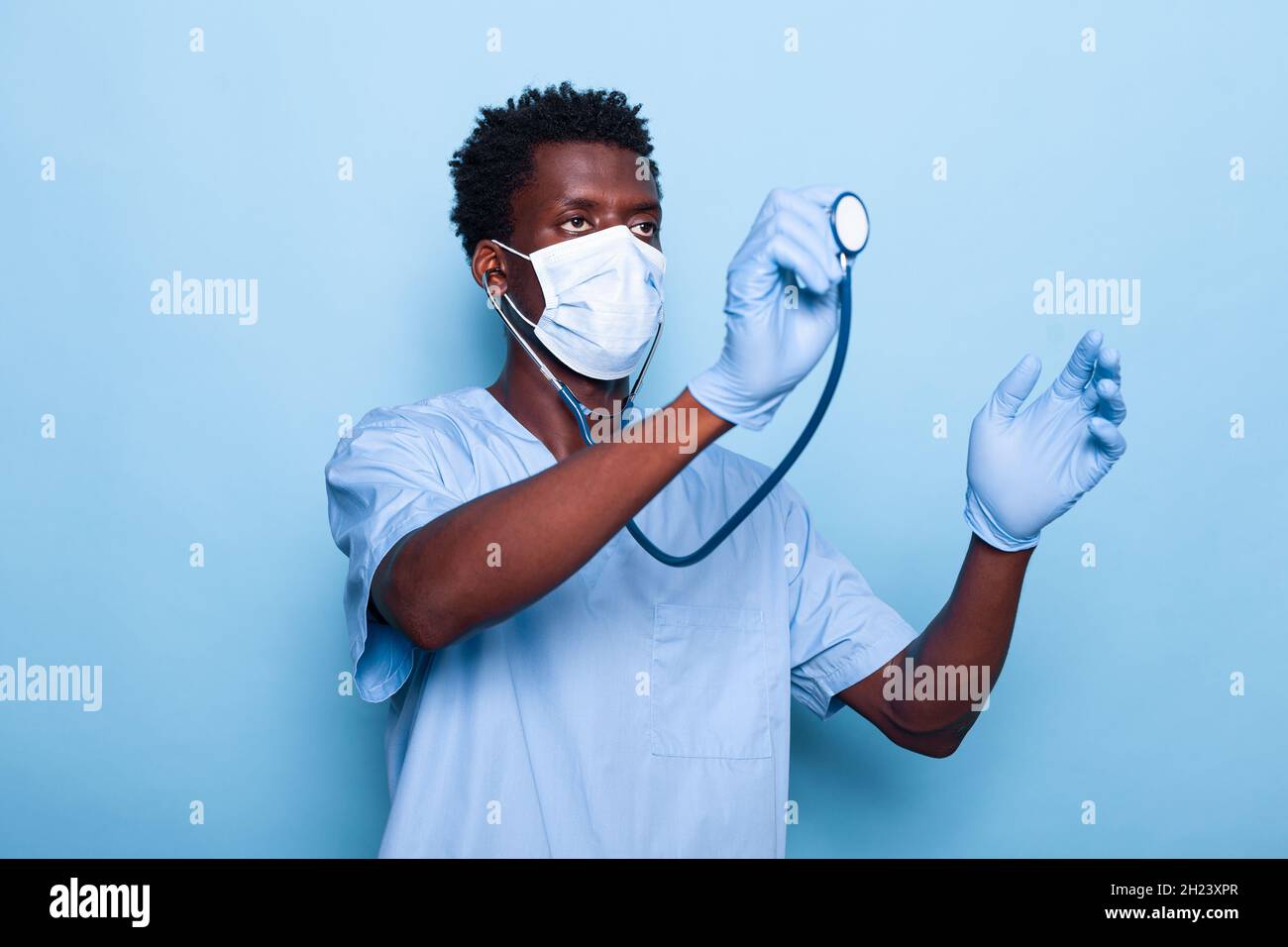 Pflegekraft, die Stethoskop hält und für die Herzschlaguntersuchung der Kardiologie verwendet. Mann Kardiologe mit medizinischen Instrument trägt Gesichtsmaske und Handschuhe gegen Coronavirus Pandemie Stockfoto
