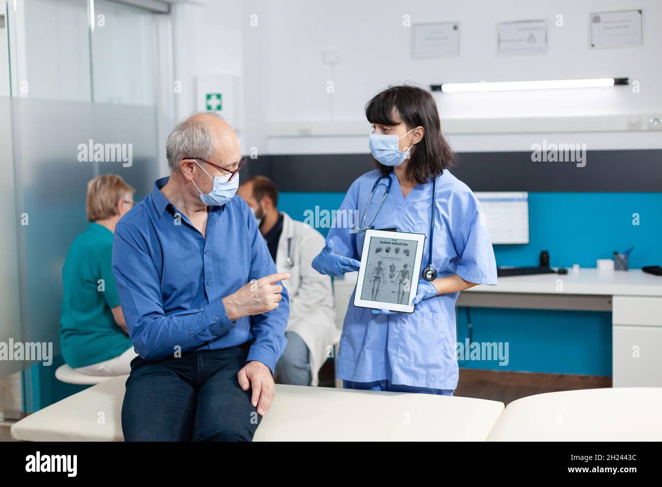 Krankenschwester, die ein digitales Tablet mit menschlichem Skelett auf dem Bild eines älteren Patienten hält. Medizinische Assistentin erklärt Osteopathie Diagnose und Rehabilitation mit Gerät, um pensionierten Mann zu heilen. Stockfoto