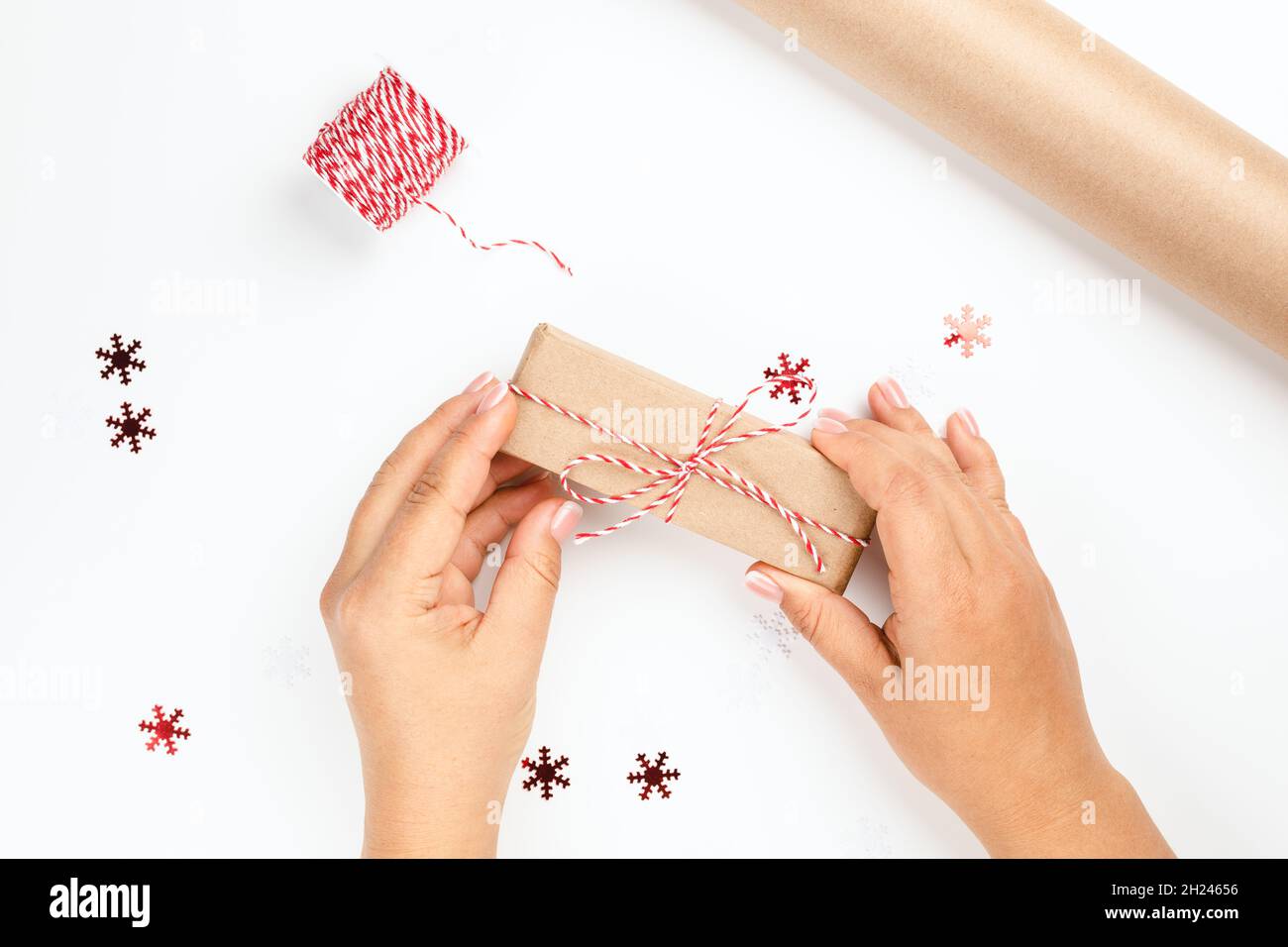 Neujahrskarte mit Frauenhänden, die Geschenkbox und Verpackungsausrüstung auf dem Tisch halten - Rolle mit rotem Faden und Rolle Bastelpapier Stockfoto