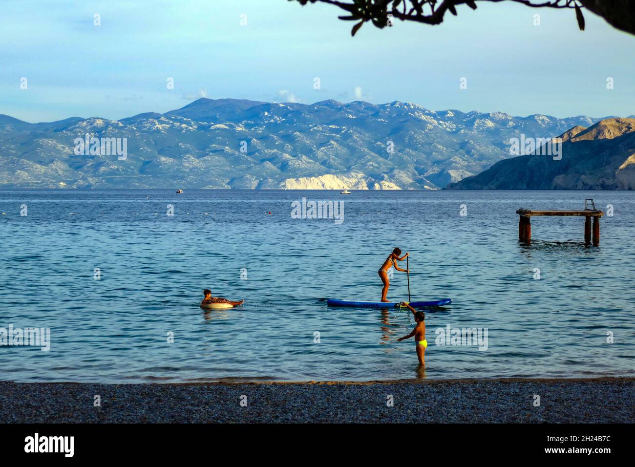 Paddleboarding für Familien mit ruhiger Strandszene im kleinen Ferienort Baska, Baška auf der Insel Krk, Kroatien Stockfoto