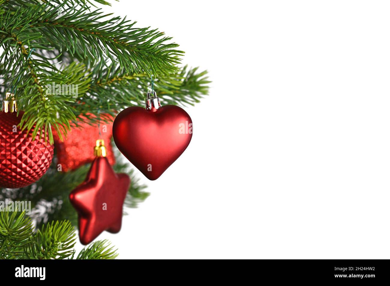 Rote herzförmige Weihnachtskugel auf geschmücktem Weihnachtsbaum auf weißem Hintergrund mit Kopierraum Stockfoto