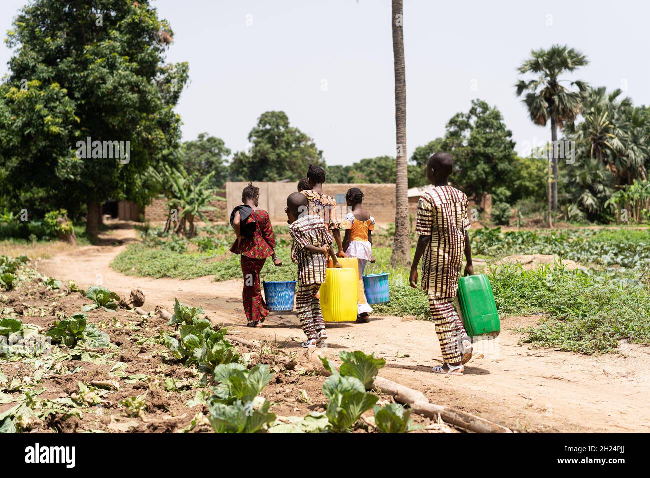 Eine Gruppe schwarzafrikanischer Kinder, die mit leeren Wasserbehältern nach Hause gehen, nachdem sie ihrem Vater geholfen haben, das Familienfeld zu bewässern Stockfoto