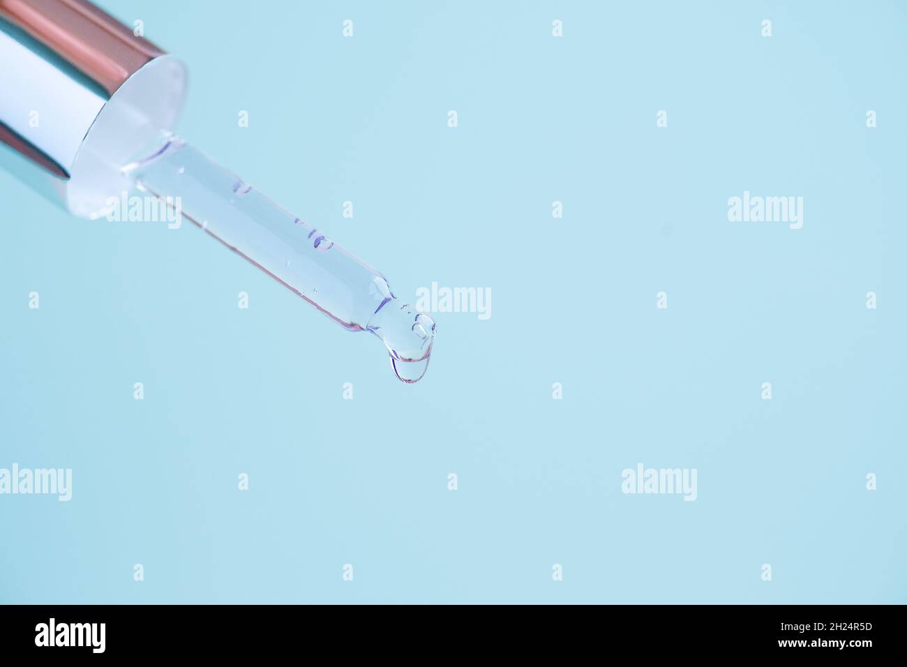 Transparente Glaspipette mit Metalldeckel, Serumflüssigkeit tropft auf blauen Hintergrund. Stockfoto