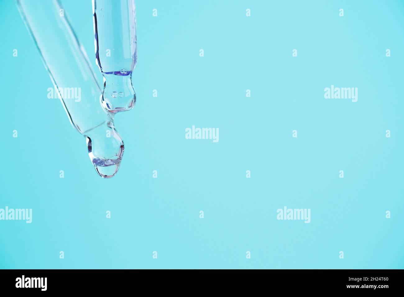 Transparente Glaspipetten mit einer Serumflüssigkeit, die auf blauen Hintergrund tropft. Stockfoto