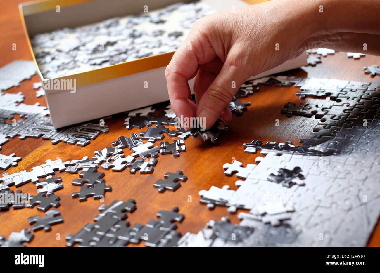 Ältere weibliche Person tut Puzzle auf Holztischplatte Stockfoto