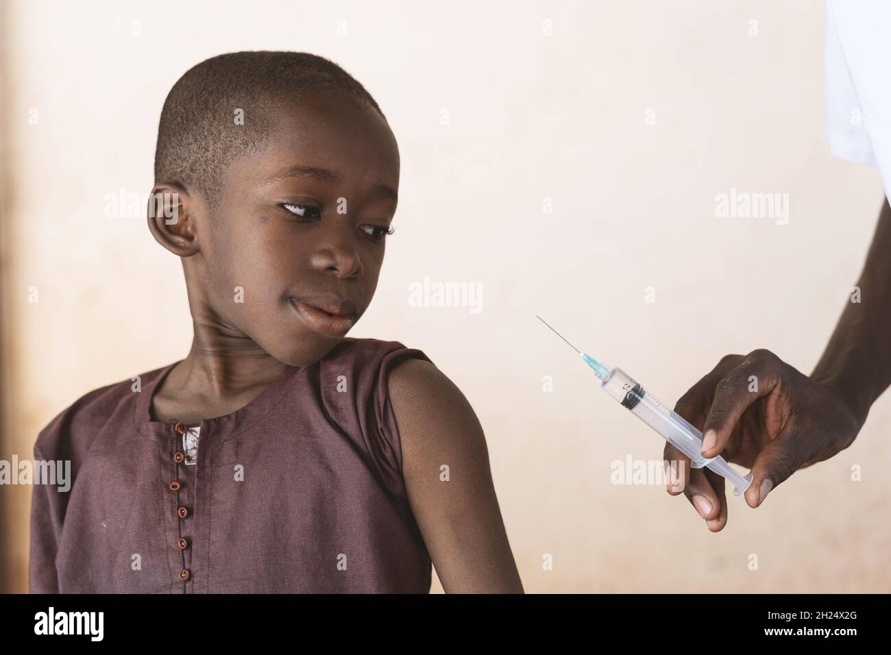 Medizinisches Fachpersonal, das eine Spritze mit Malariaimpfstoff hält, die einem kleinen schwarzen afrikanischen Jungen im Rahmen eines Malariakontrollprogramms injiziert werden soll - Stockfoto