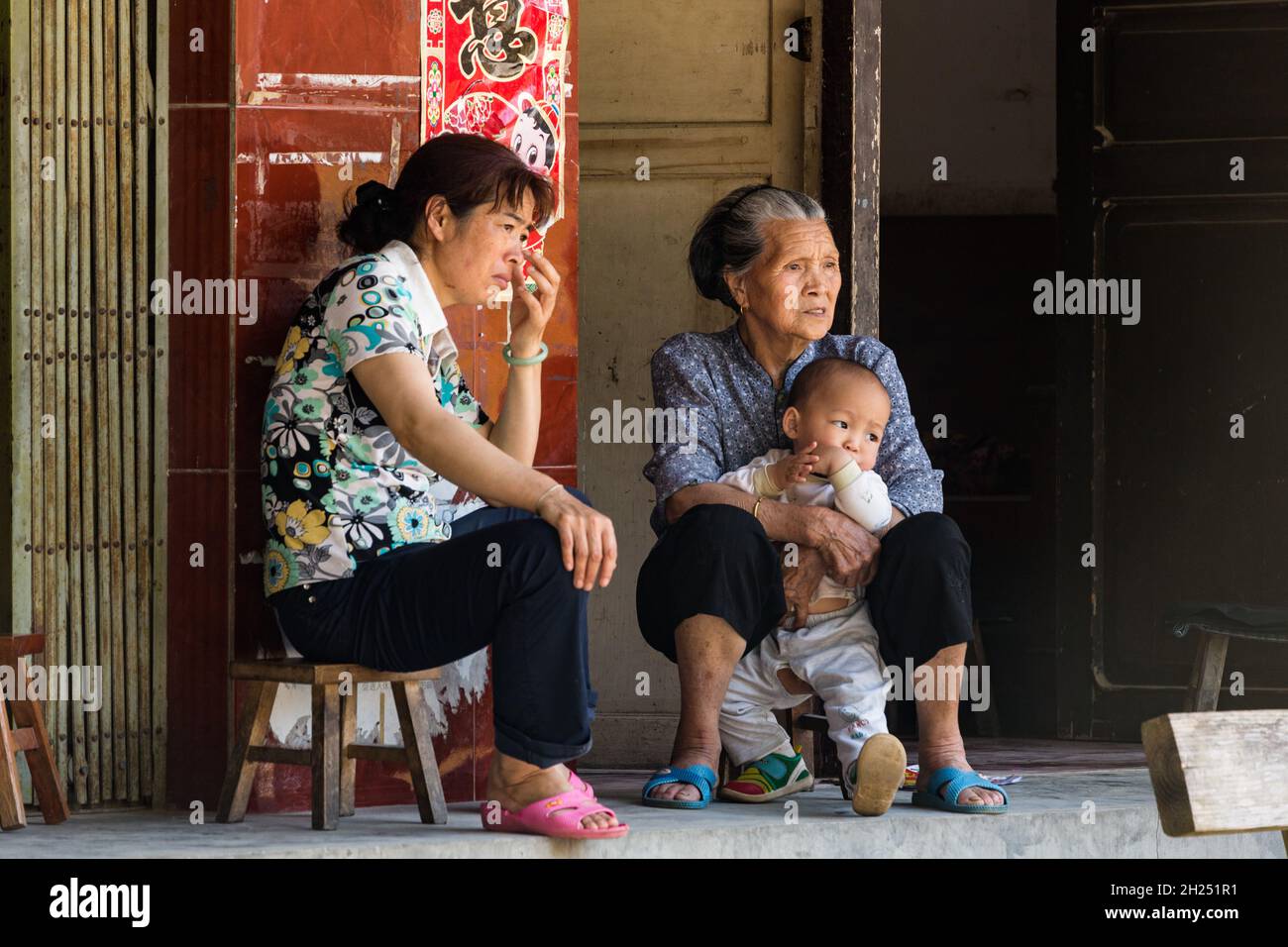 Drei Generationen einer chinesischen Familie sitzen auf Hockern vor ihrem Haus in Huangluo, China. Stockfoto
