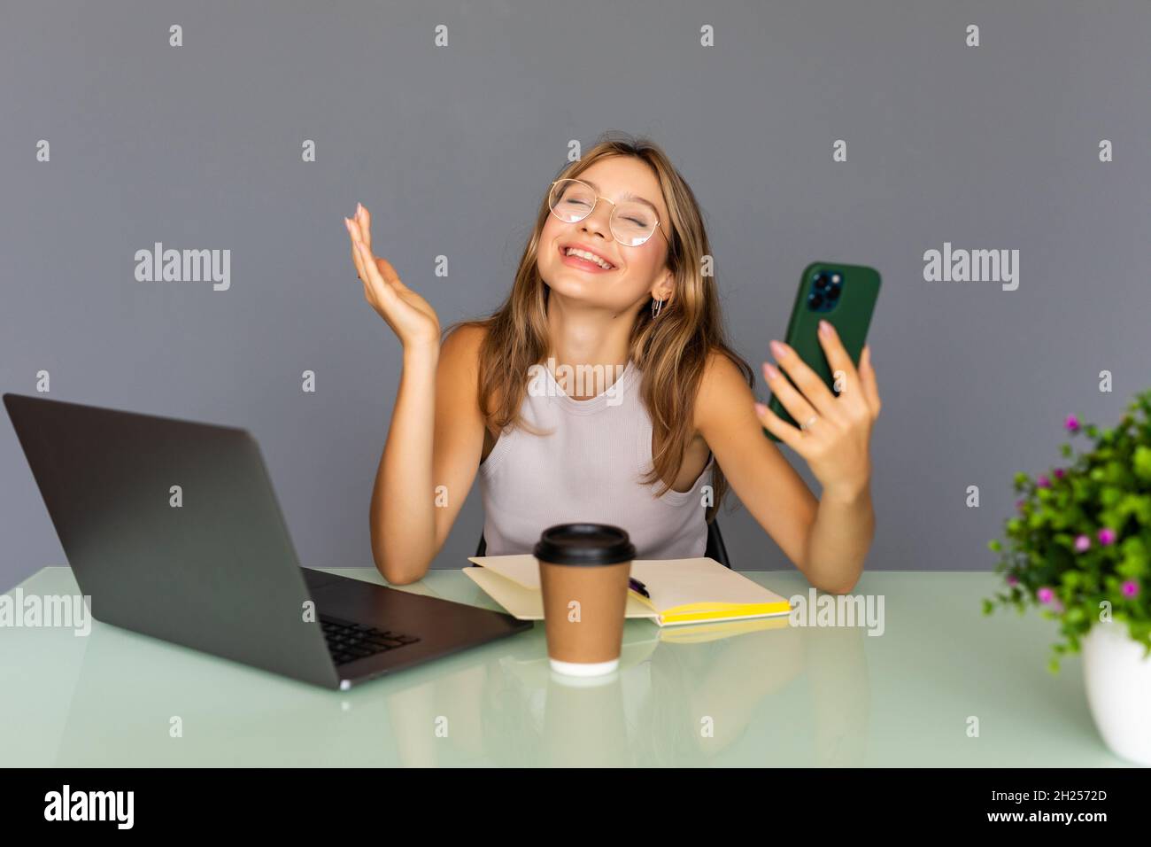 Gute Nachrichten. Schöne glückliche junge moderne Geschäftsfrau nutzt ihr Telefon, während sie im Startup-Büro arbeitet Stockfoto