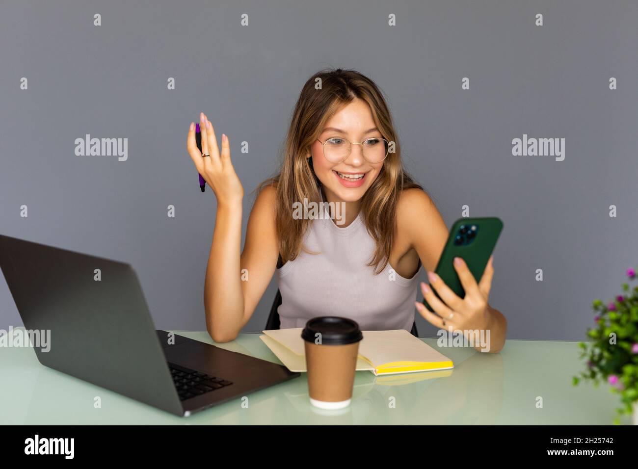 Gute Nachrichten. Schöne glückliche junge moderne Geschäftsfrau nutzt ihr Telefon, während sie im Startup-Büro arbeitet Stockfoto