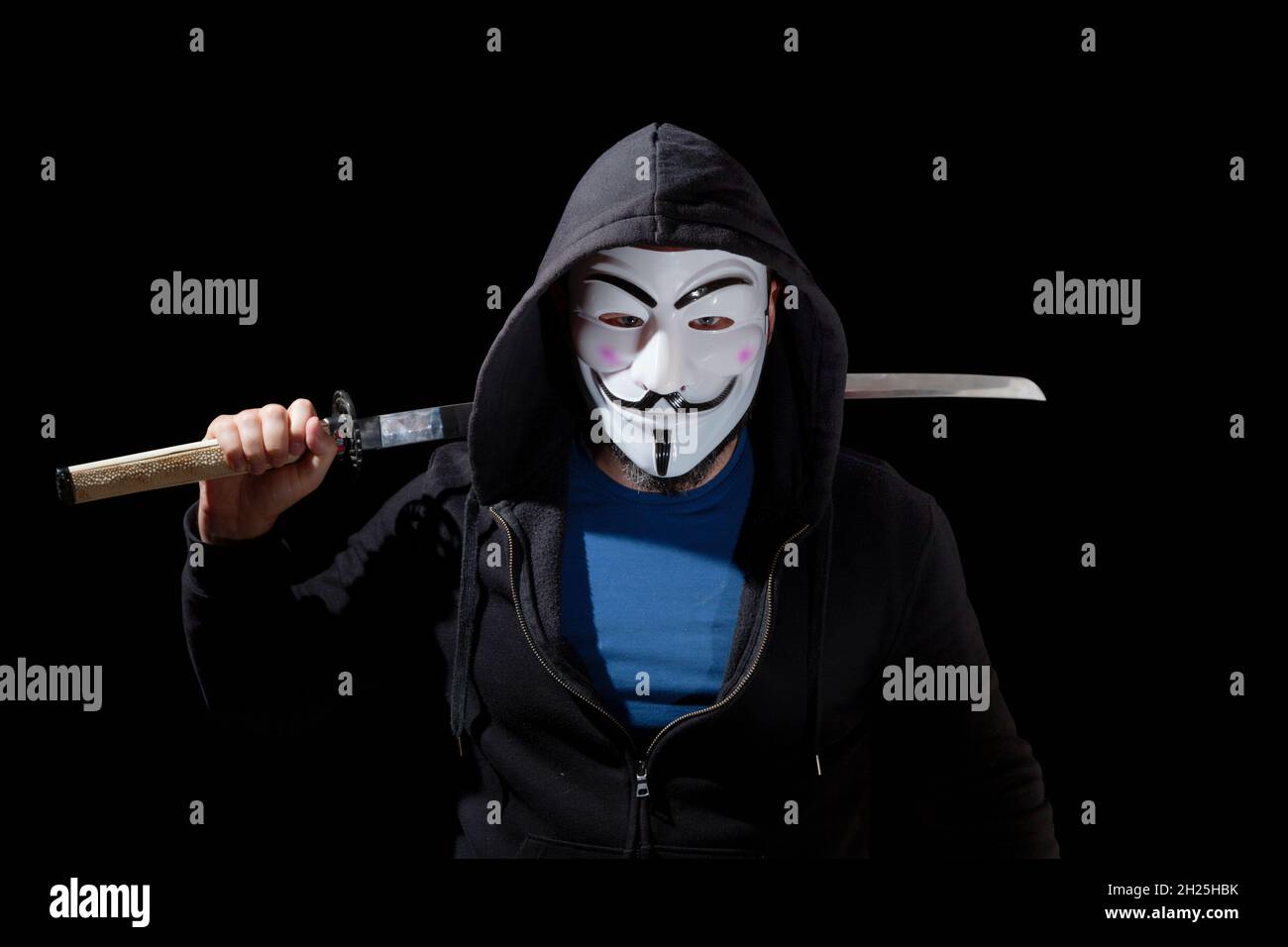 Mann, der mit einem Katana bewaffnet ist und eine Maske und einen Hoodie auf schwarzem Hintergrund trägt. Stockfoto