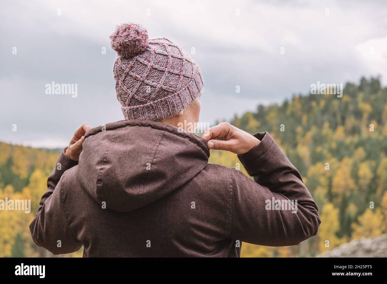 Eine weibliche Reisende steht auf dem Gipfel des Berges und bewundert die herrliche Landschaft des Herbstwaldes von oben. Selektiver Fokus. Nahaufnahme. Stockfoto