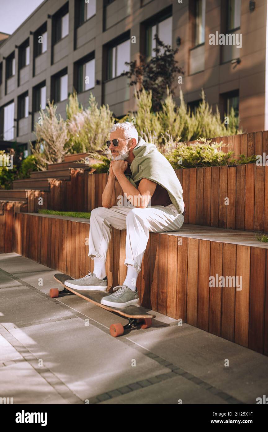 Männlicher Skateboarder mit seinen Füßen auf dem Skateboard draußen sitzen Stockfoto