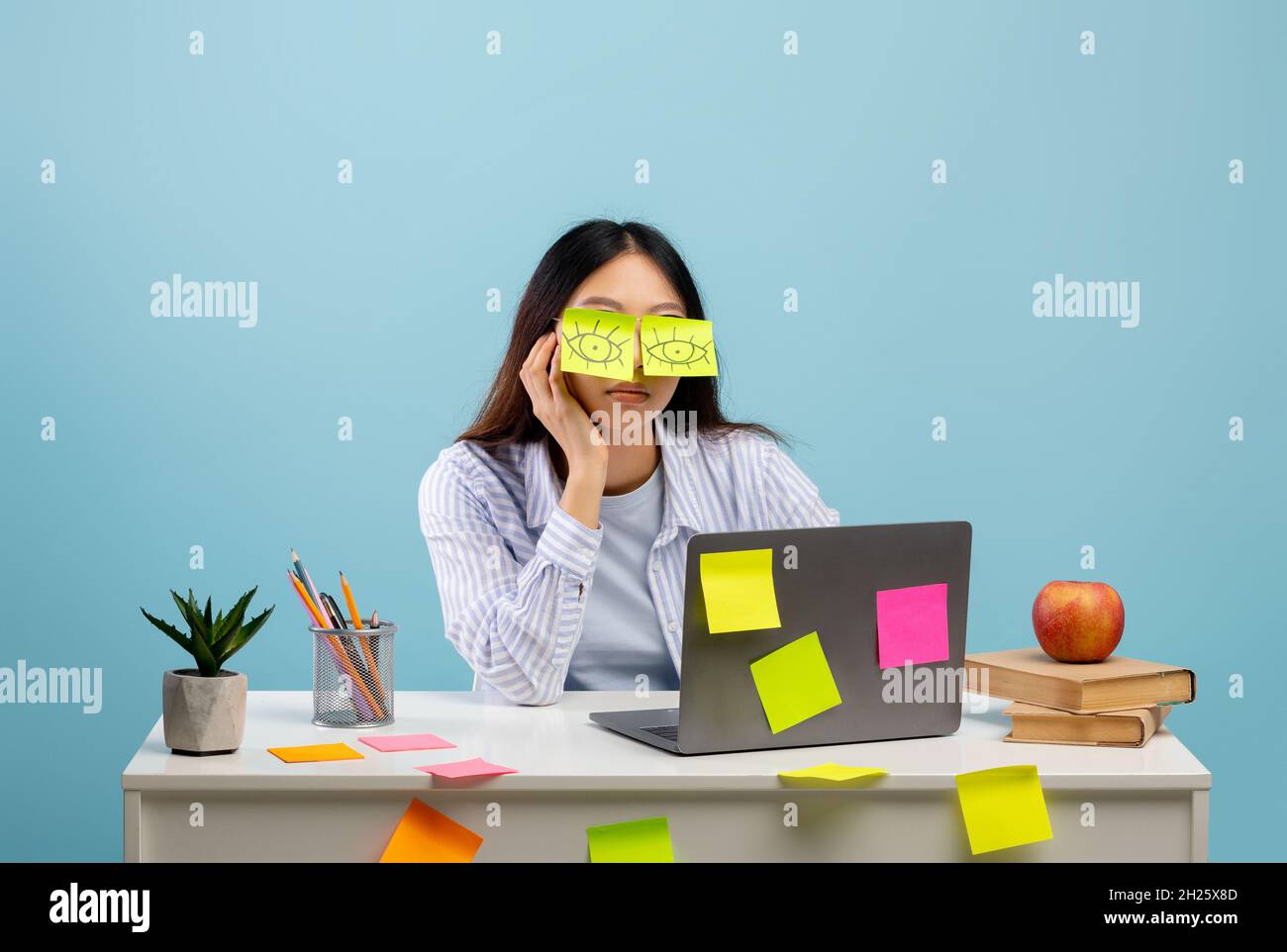 Viel Arbeit Konzept. Müde asiatische Studentin schlafen mit Aufklebern auf den Augen, sitzen am Tisch über blauem Hintergrund Stockfoto