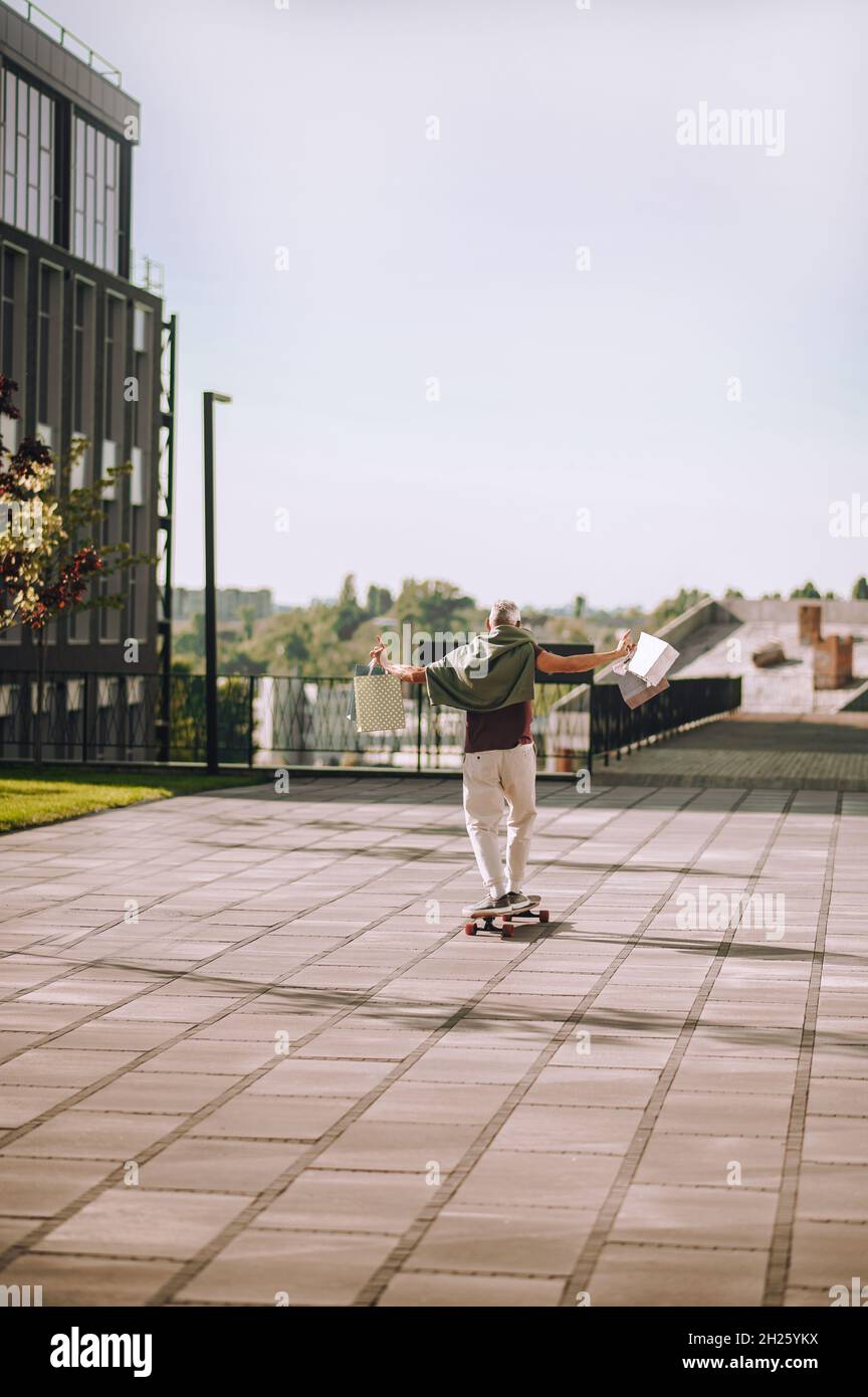 Mann mit Käufen in den Händen, der auf dem Skateboard steht Stockfoto