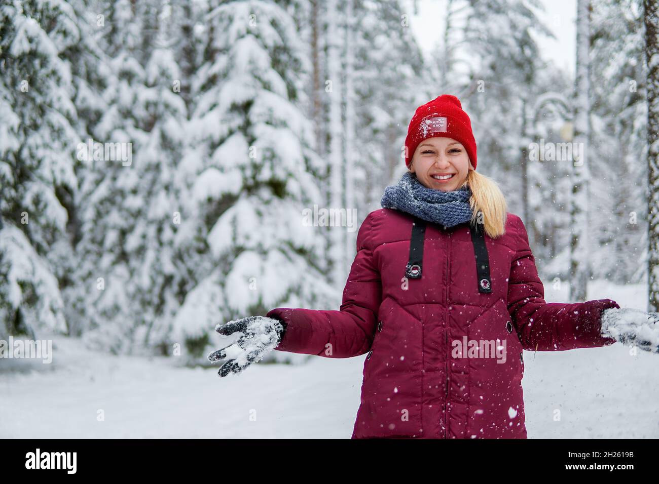 Teenagermädchen in einer roten Jacke, die Schnee wirft und in einem verschneiten Wald lacht. Stockfoto