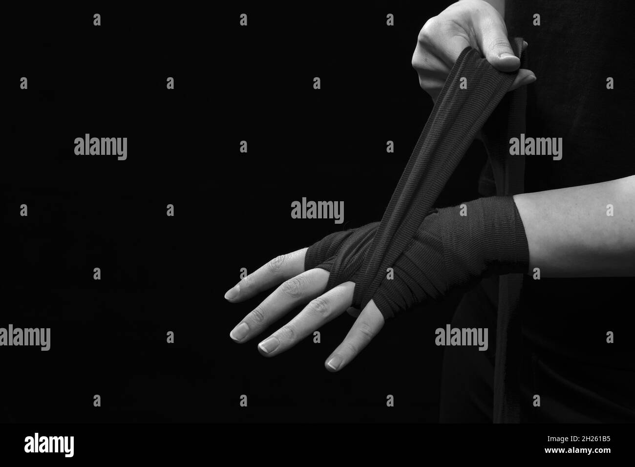 Muay Thai Boxerin mit Trageschlaufe am Handgelenk Nahaufnahme. Fitness junge Frau Vorbereitung für das Boxtraining auf schwarzem Hintergrund, monochrom Stockfoto