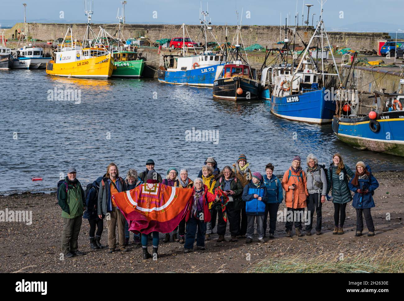 East Lothian, Schottland, Großbritannien, 20. Oktober 2021. COP26 Pilgerfahrt: Basisgruppen auf der schottischen Etappe eines Spaziergangs zur COP26. Die Teilnehmer, die sich auf dem Weg anschließen, glauben, dass die COP26 nicht die wesentlichen Veränderungen herbeiführen wird, die zur Bekämpfung des Klimawandels erforderlich sind. Die Route heute ist auf dem John Muir Way. Im Bild: Die Gruppe am Hafen von Port Seton mit Fischerbooten, die bei Ebbe auf Grund liegen Stockfoto