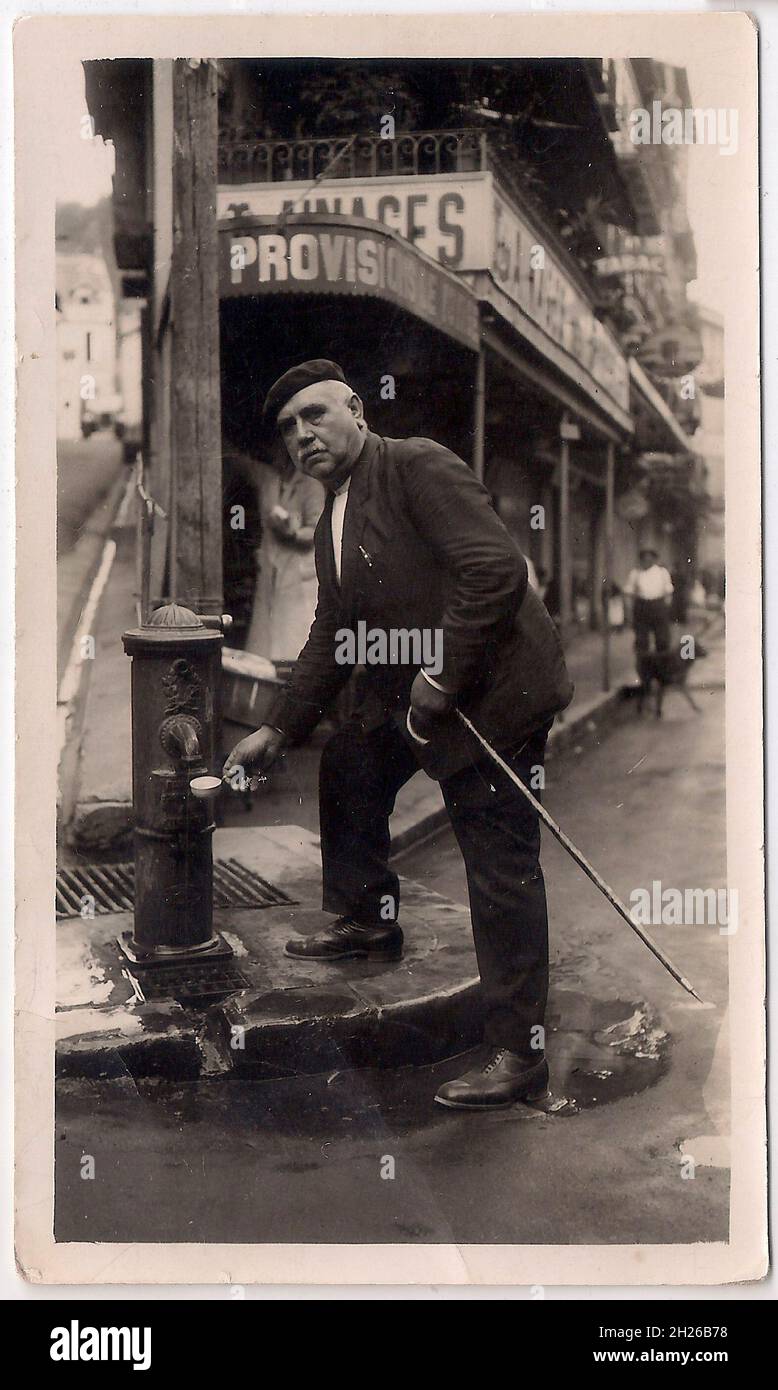 Vintage-Foto eines älteren Franzosen, der Wasser an einer öffentlichen Pumpe trinkt (Anfang 20. Jahrhundert) Stockfoto