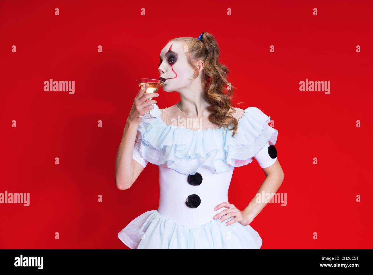 Mystische blonde Frau in halloween Make-up und gruselige Gesichtsausdruck trinken Wein isoliert über rotem Hintergrund Stockfoto