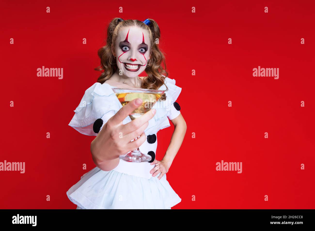 Mystische blonde Frau in halloween Make-up und gruselige Gesichtsausdruck trinken Wein isoliert über rotem Hintergrund Stockfoto