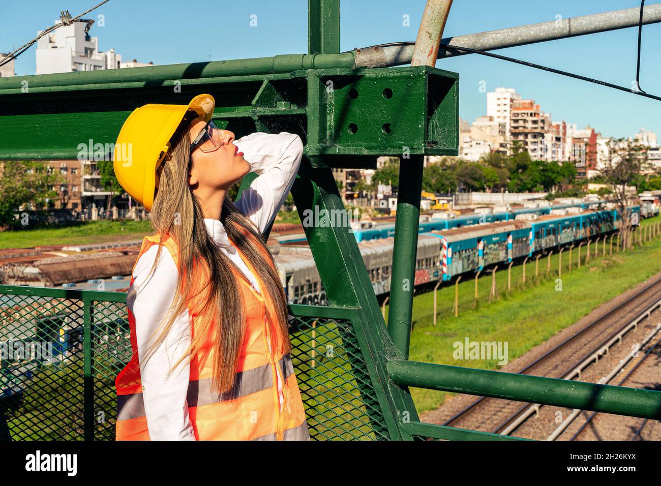 Schöne junge Ingenieurin oder Aufsichtsperson, trägt Sicherheitsausrüstung, inspiziert eine Eisenbahn Fußgängerbrücke. Konzept der ermächtigten Frau, Beruf Stockfoto
