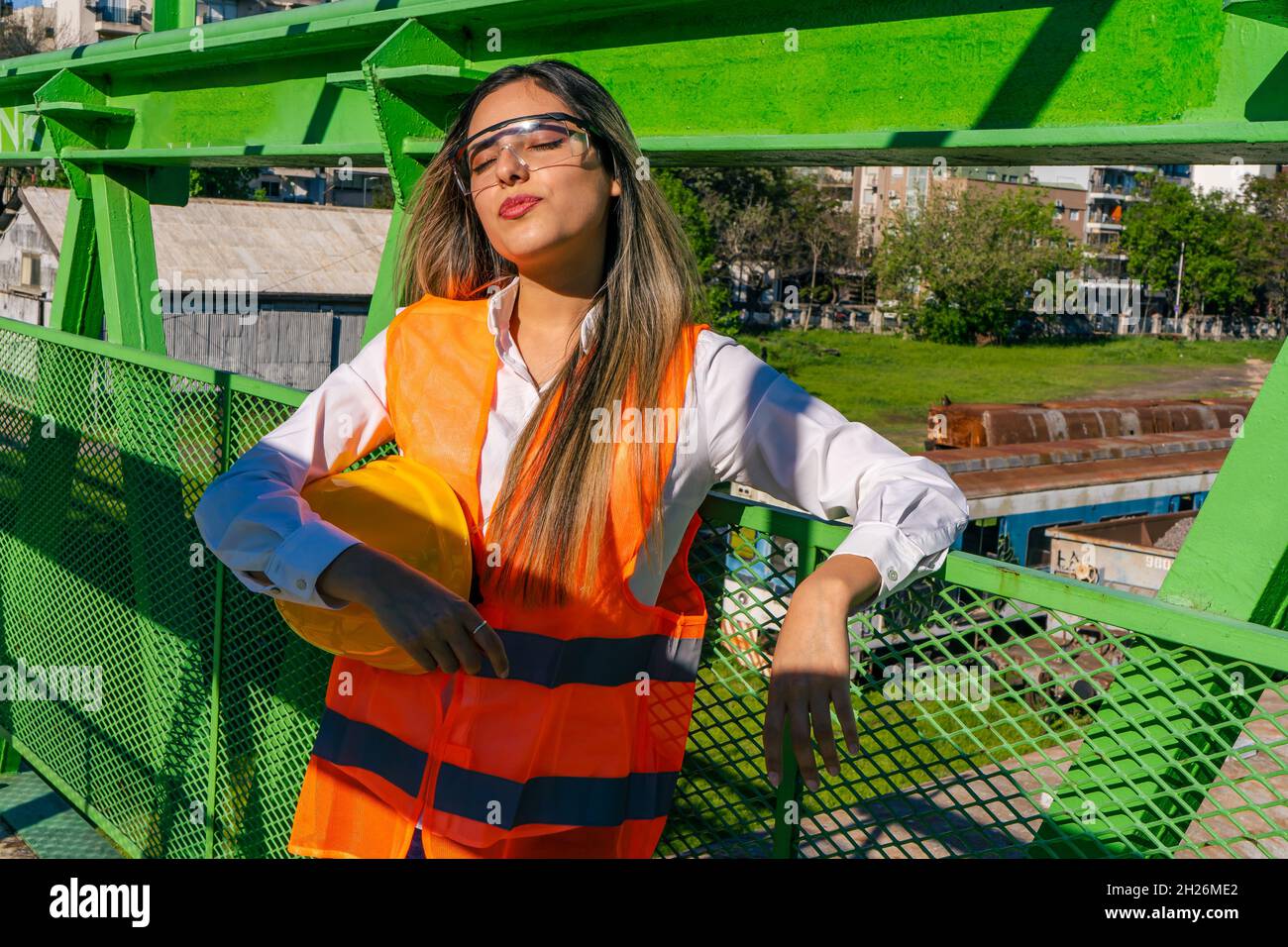 Schöne junge Ingenieurin oder Aufsichtsperson, die Sicherheitsausrüstung trägt, in der Sonne ruht, während sie auf Arbeiter wartet. Konzept der ermächtigten Frau, Beruf Stockfoto
