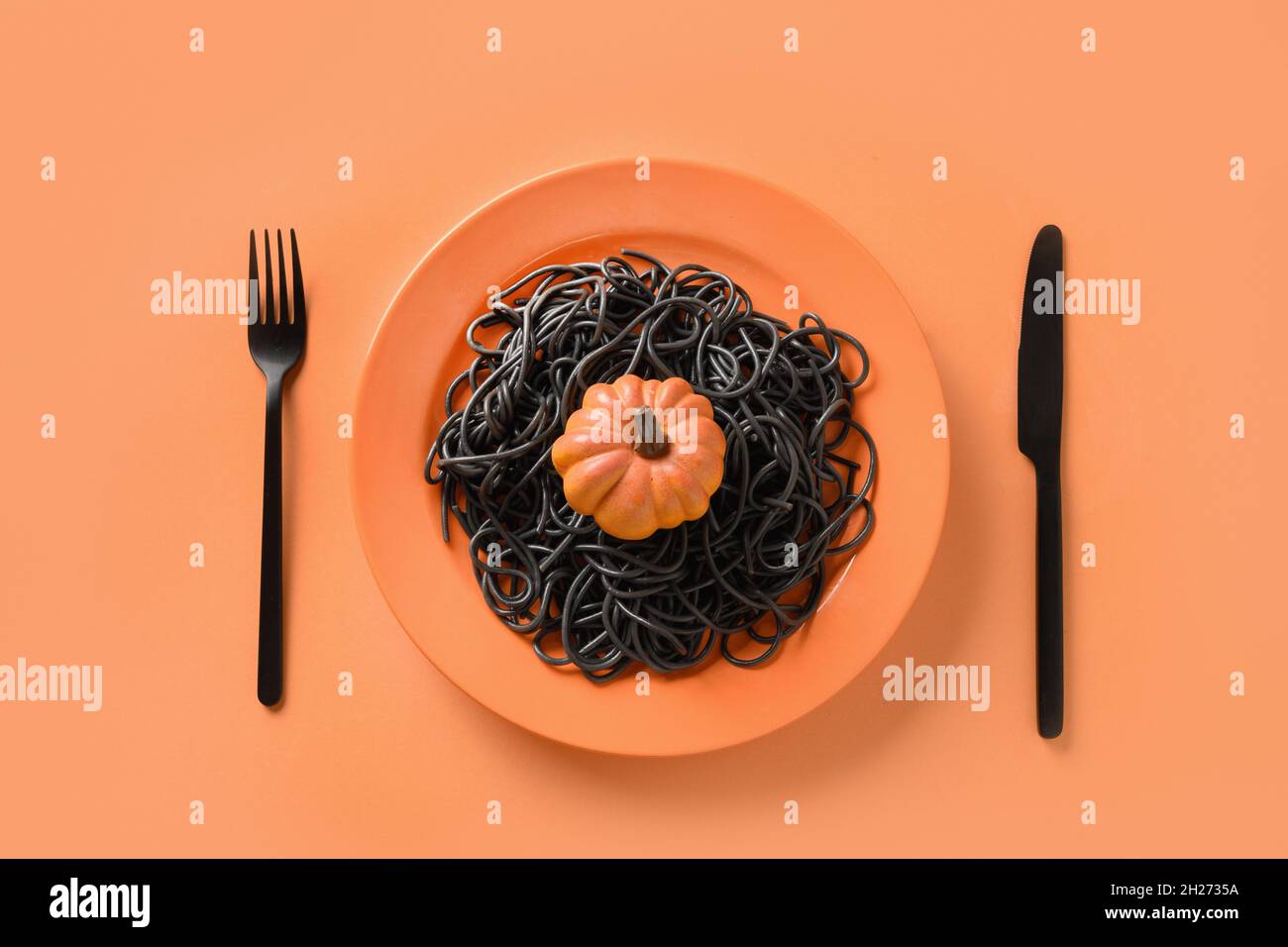 Halloween kreative italienische schwarze Pasta Tintenfisch Tinte verziert Kürbis in orange Platte auf weißem Hintergrund. Blick von oben. Lebensmittelkonzept. Lustige Tischset Stockfoto
