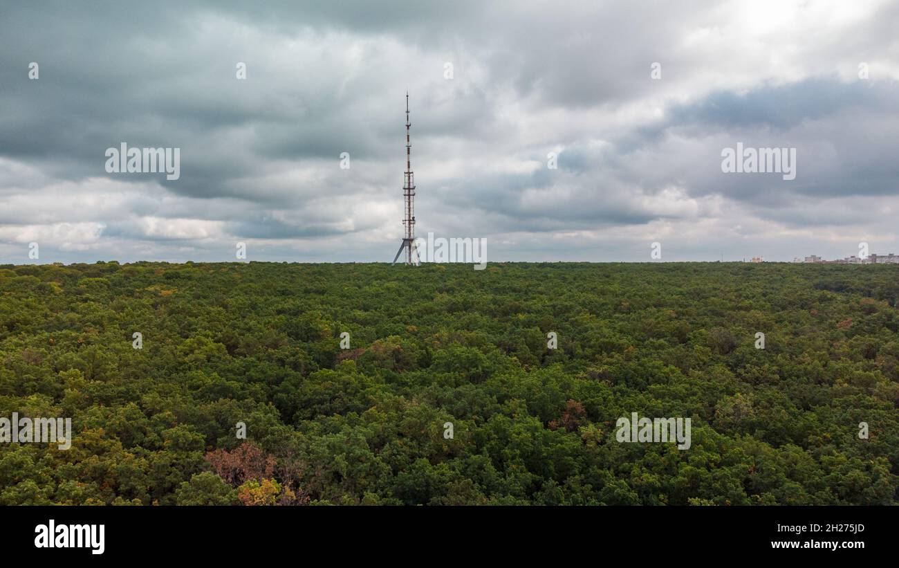 Luftaufnahme grüner dunkler Wald mit Telekommunikationsturm-Antenne und wolkig grauem epischen Himmel. Charkiw, Ukraine Stockfoto