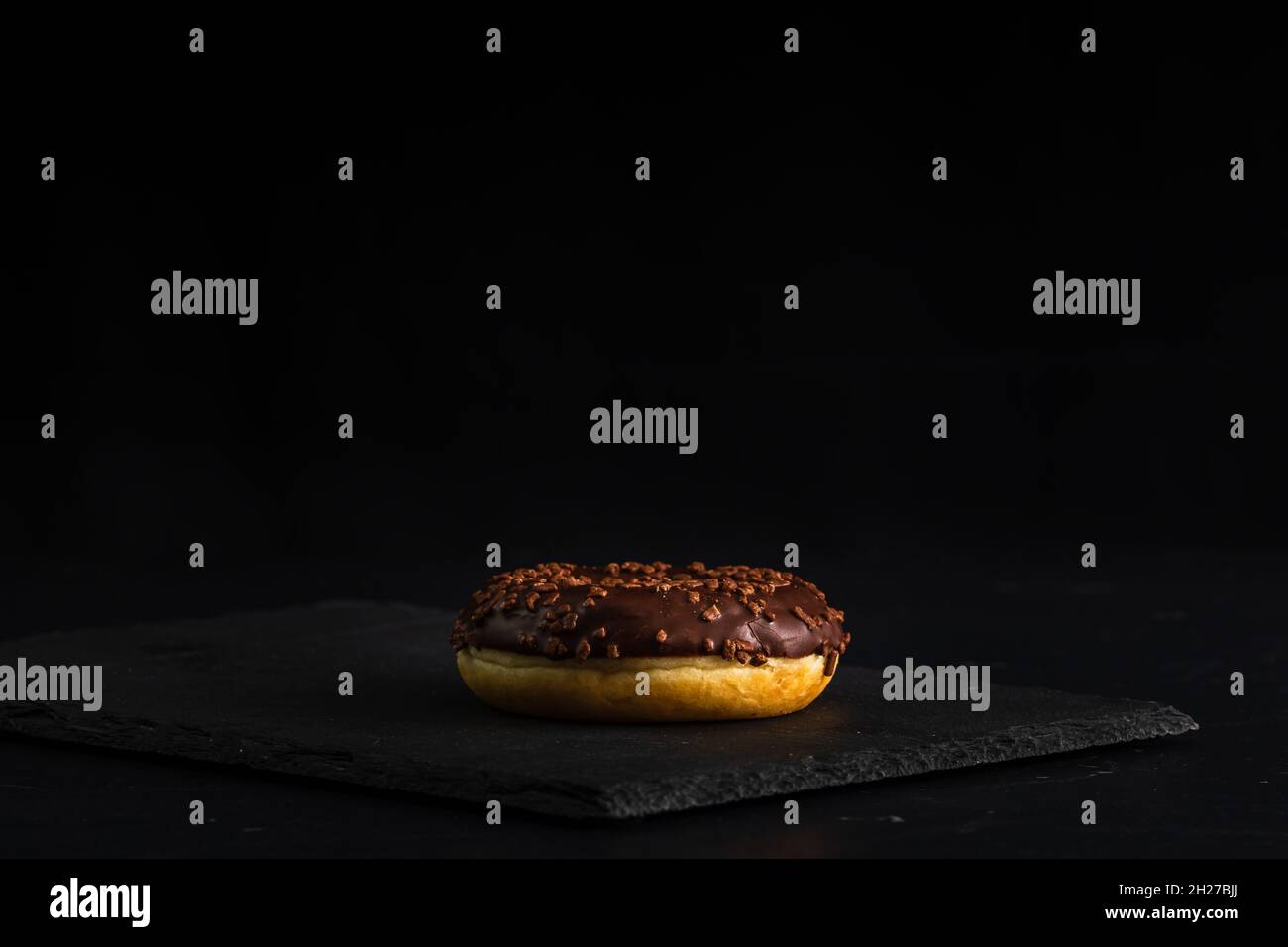 Nahaufnahme eines frischen, schokoladigen Donuts mit Nüssen, isoliert auf schwarzem Hintergrund Stockfoto