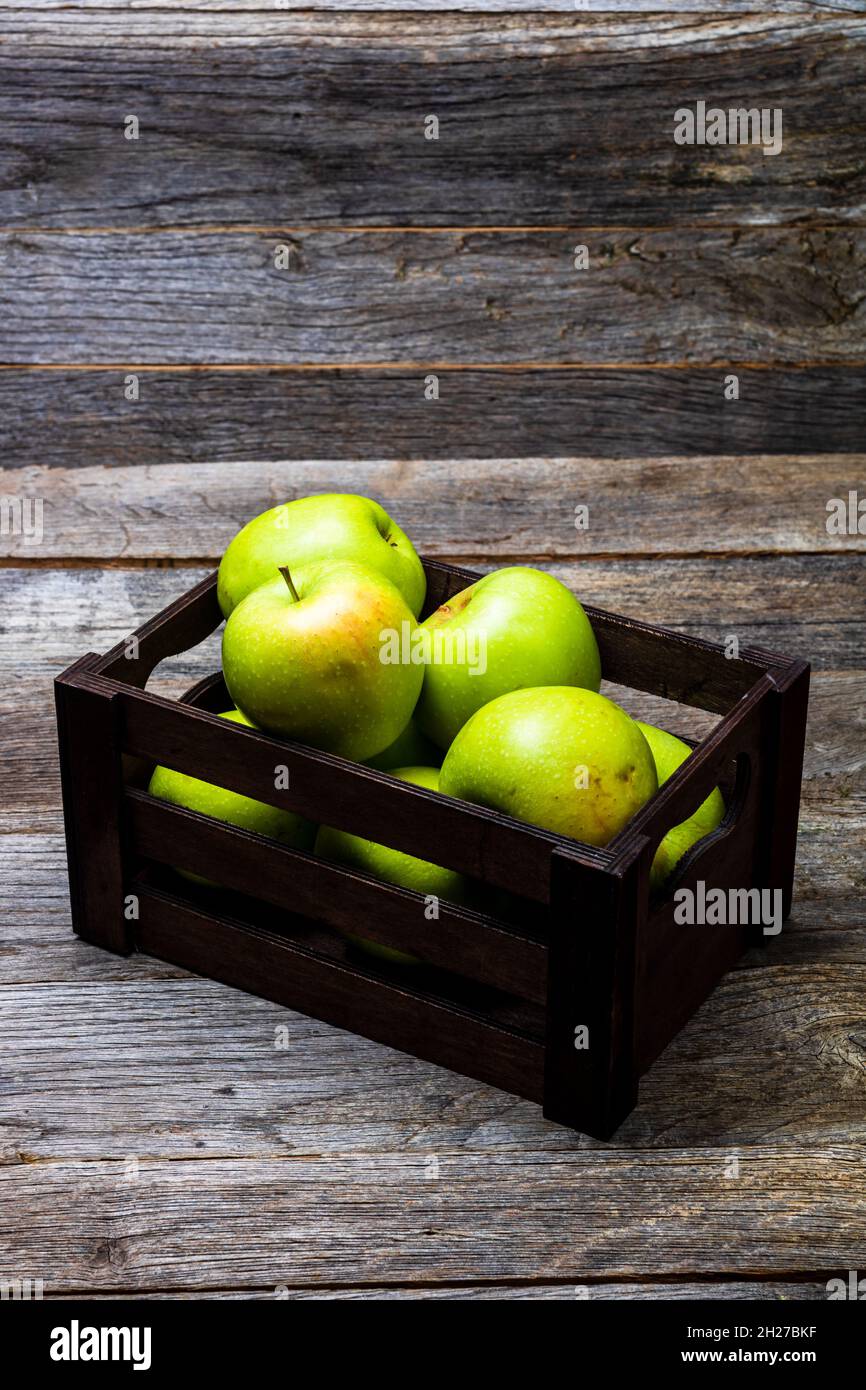 Vertikale Nahaufnahme einer schwarzen Kiste mit reifen grünen Äpfeln, isoliert auf einem Holztisch Stockfoto