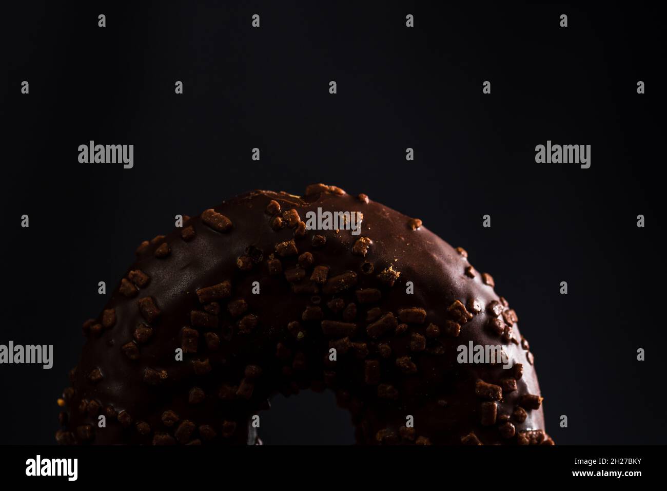 Nahaufnahme eines frischen, schokoladigen Donuts mit Nüssen, isoliert auf schwarzem Hintergrund Stockfoto
