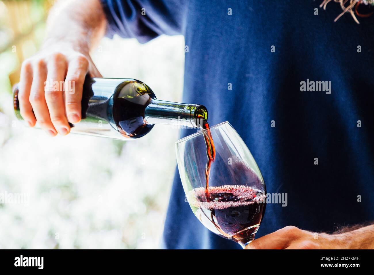 Ein junger Mann mit einer Flasche, der Wein in ein Glas gießt. Stockfoto