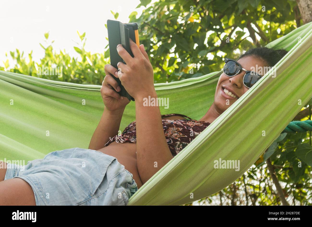 Schöne dunkelhäutige Frau liest in einer Hängematte am Meer Stockfoto